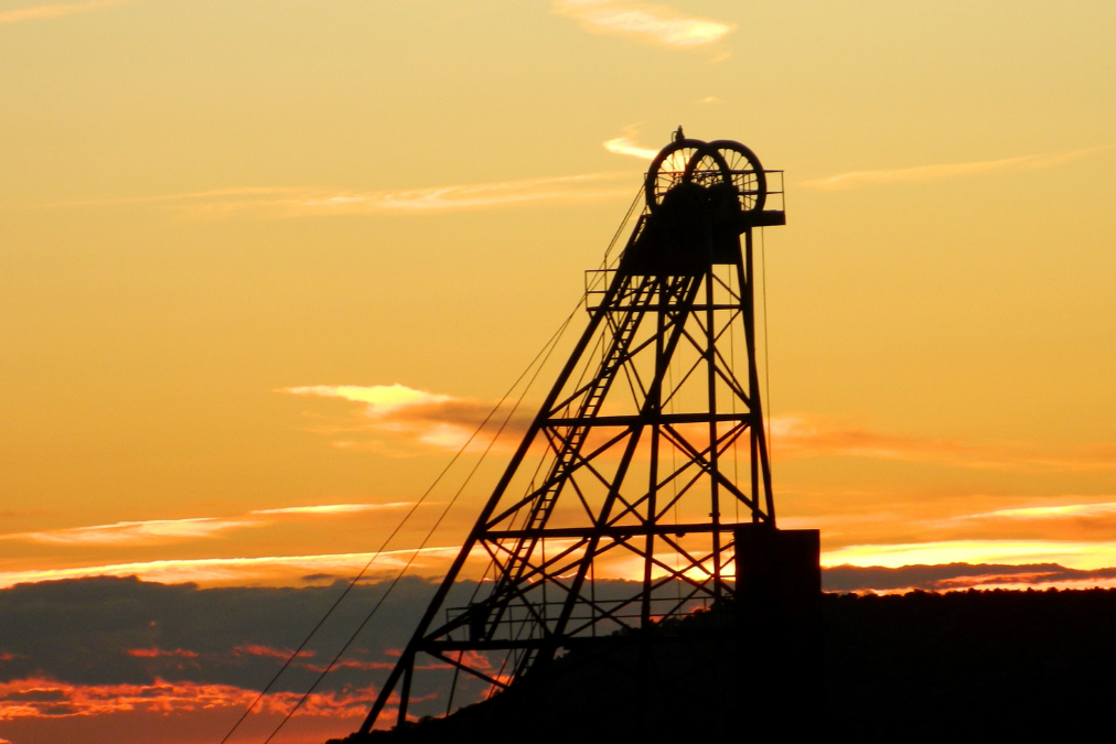 Silhouette of a mine headgear structure against a golden sunset sky, symbolising the transition from mining heritage to new opportunities.